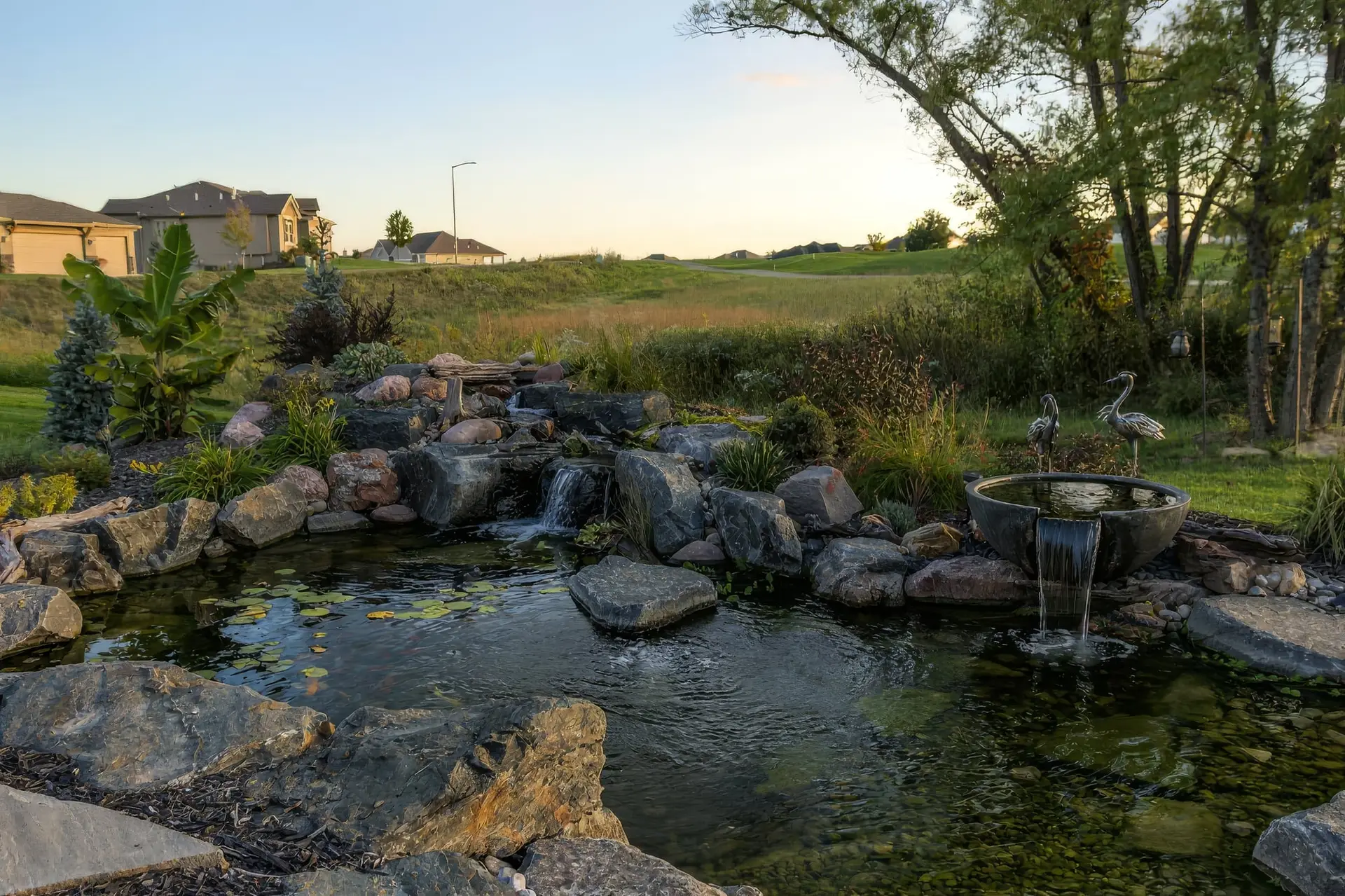 A wide backyard pond with a waterfall under a summer sky